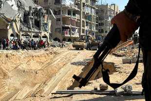 Ein Gewehr in der Hand vor einer Baustelle in Gaza