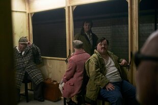 Ein holzgezimmerter Wagon mit Fahrgästen, einer trägt einen Karomantel und Mütze wie ein Detektiv