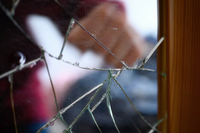 Ein zerbrochenes Fenster mit schemenhafter Hand dahinter