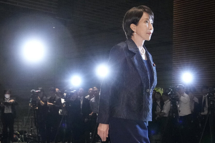 Sanae Takaichi verlässt ein Gebäude, sie trägt schwarz, es ist Nacht und im Hintergrund ist ein Reihe Journalist*innen zu sehen