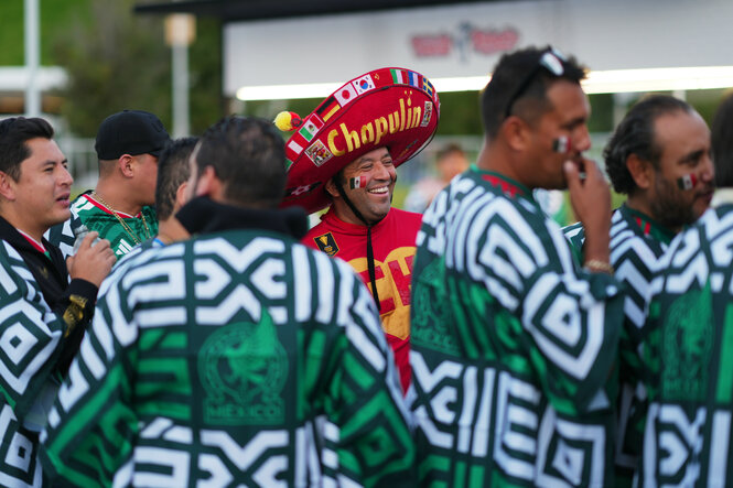 Männer mit Ponchos, einer mit Sombrero, stehen gut gelaunt am Rande eines Fußballspiels