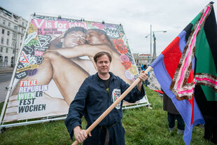 Milo Rau schwenkt eine bunte Fahne