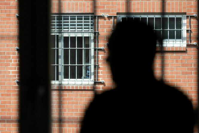 Eine schwarze Silhouette einer Person vor vergittertem Fenster