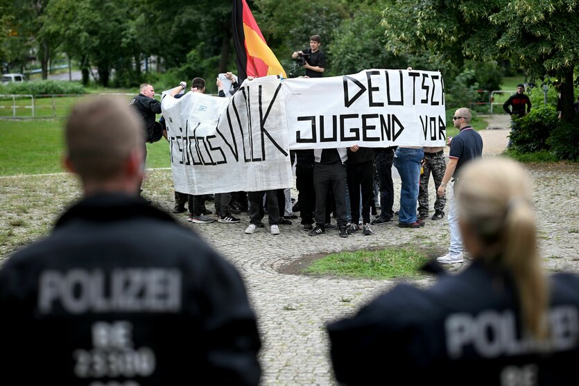 Eine Gruppe junger Nazis mit dem Banner "Deutsche Jugend Voran" wird von zwei Polizisten beobachtet