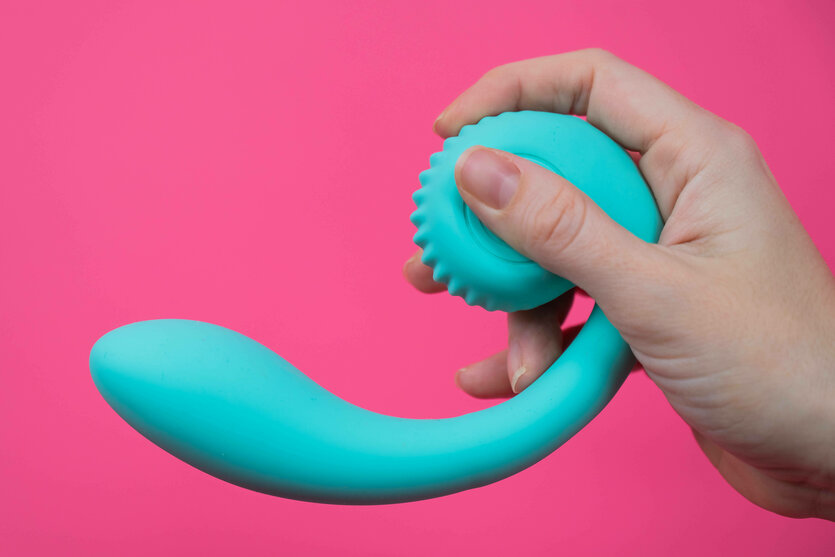 Hand hält blaues, gebogenes Sexspielzeug auf rosa Hintergrund