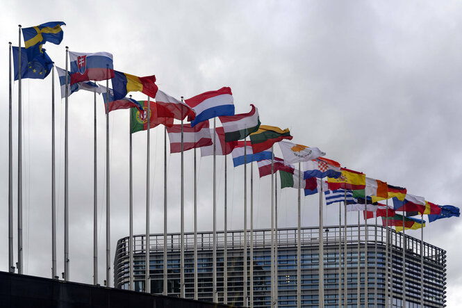 Die Flaggen der EU Mitgliedsstaaten wehen kräftig im Wind vor dem Parlament