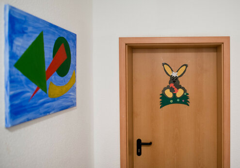 Eine Zimmertür mit aufgeklebtem buntem Hasen, daneben ein Bild aus geometrischen Formen