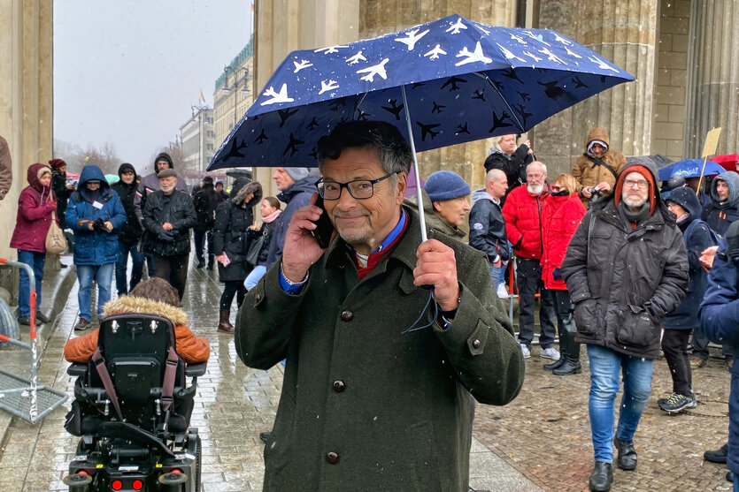 Diether Dehm telefonierend und mit Regenschirm