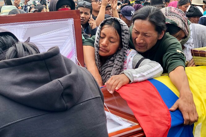 Zwei Menschen stehen an einem Sarg, über dem die ecuadorianische Flagge liegt