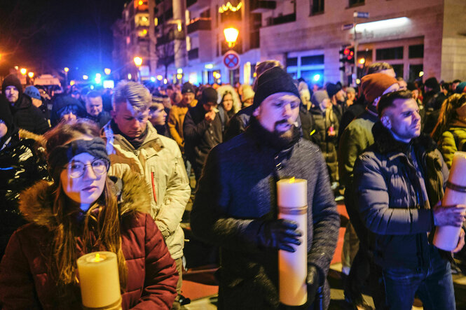 Eine Menschenmenge steht auf einem Platz, es ist dunkel, einige Menschen tragen große Kerzen