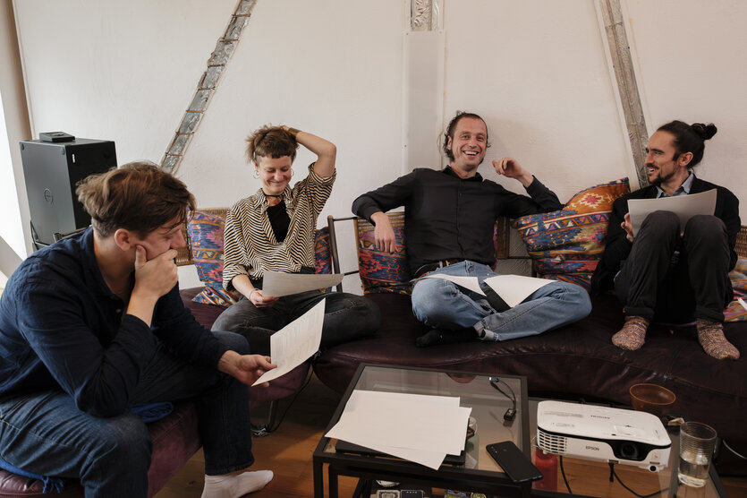 Vier Menschen sitzen in einer Wohnung auf einer Couch und diskutieren