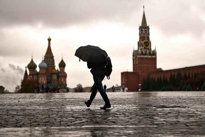 Ein Mann mit Regenschirm läuft über den Roten Platz in Moskau