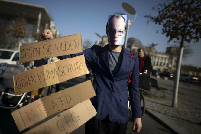 Ein Demonstrant mit Merz Make und Schild: Gegen Schulden, gegen Klimaschutz, Mit AfD