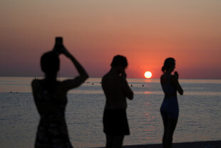 Eine Gruppe von Menschen praktiziert Yoga bei Sonnenaufgang am Strand.
