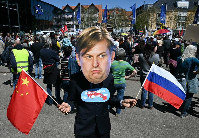 Gegner der Partei AfD demonstriert mit einer Maske des AfD Spitzenkandidaten Krah für die Europawahl und Fahnen von China und Russland vor dem AfD-Versammlungsort