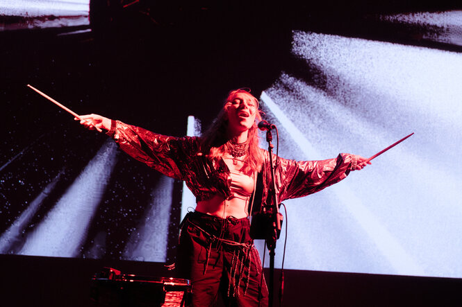 Die Musikerin Donbasgrl steht im roten Kostüm mit ausgebreiteten Armen am Schlagzeug