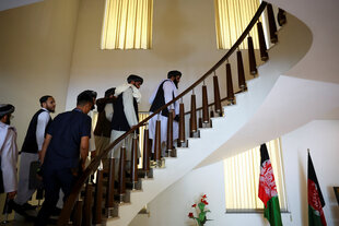 Eine Gruppe Taliban Diplomaten läuft eine geschwungene Treppe hoch