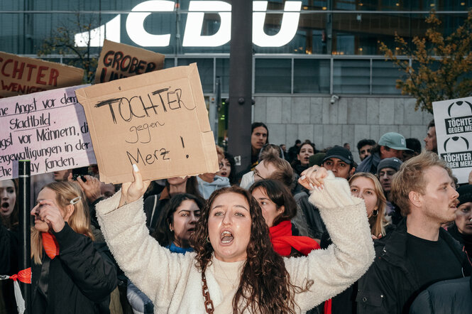 Eine Demonstrierende mit einem Protestschild, auf dem steht TÖCHTER gegen Merz!
