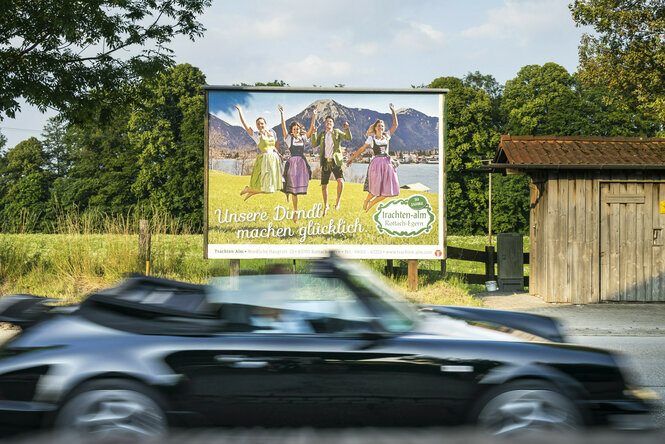 Ein Auto fährt an einer Plakatwand vorbei.