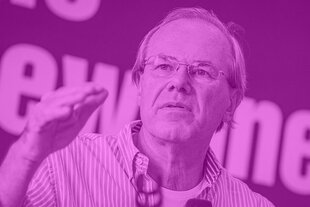 Ein älterer Mann mit Brille, Alex Demirović, spricht und hebt dabei leicht die Hand. Das Bild ist im Magentaton des Dissens-Podcasts eingefärbt, im Hintergrund sind unscharf große Buchstaben zu sehen.