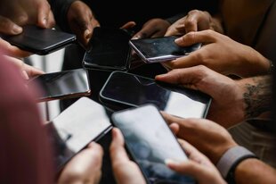 Nahaufnahme einer nicht erkennbaren Gruppe unterschiedlicher Menschen, die im Kreis stehen und über Smartphones Daten austauschen.