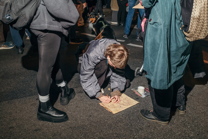 Eine gebückte Person schreibt etwas auf ein Pappschild