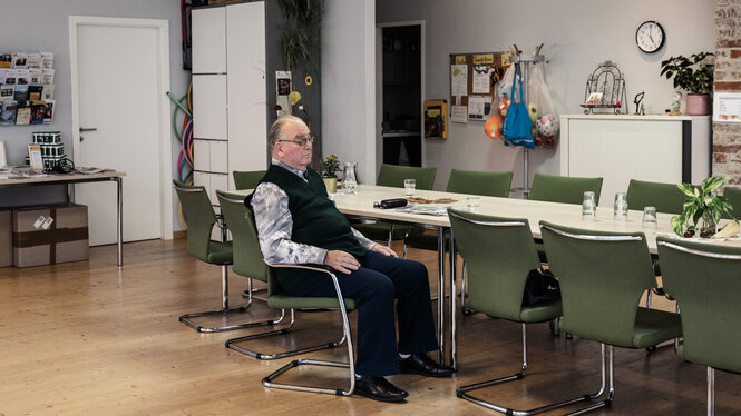 Eine Person sitzt alleine in einem Raum mit vielen Stühlen.