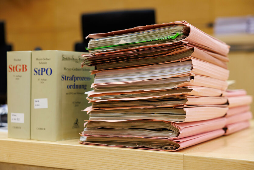 Ein Stapel Aktenordner mit Dokumenten steht auf einem Tisch neben juristischen Büchern: Strafprozessordnung und Strafgesetzbuch