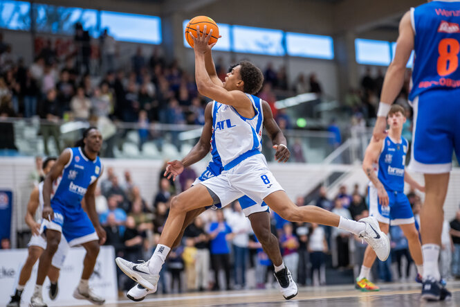 Ein junger Sportler zieht mit einem Basketball in der Hand und großen Schritten zum Korb
