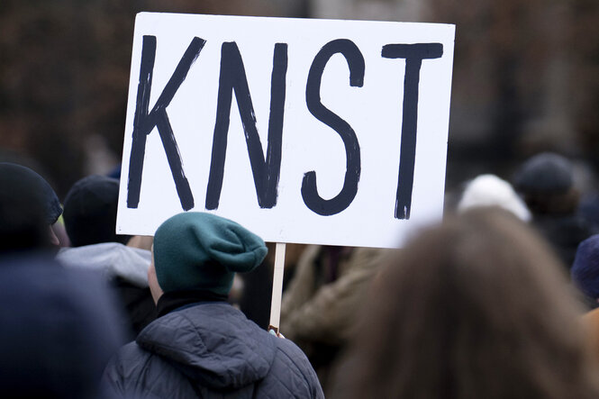 Demonstrierende halten ein Protestschild, auf dem steht KNST