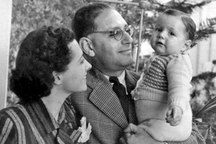 Schwarz-Weiß-Aufnahme von Michael Moos als Baby, gehalten von seinem bebrilltem Vater, links neben ihm die Mutter mit dunklen Locken.