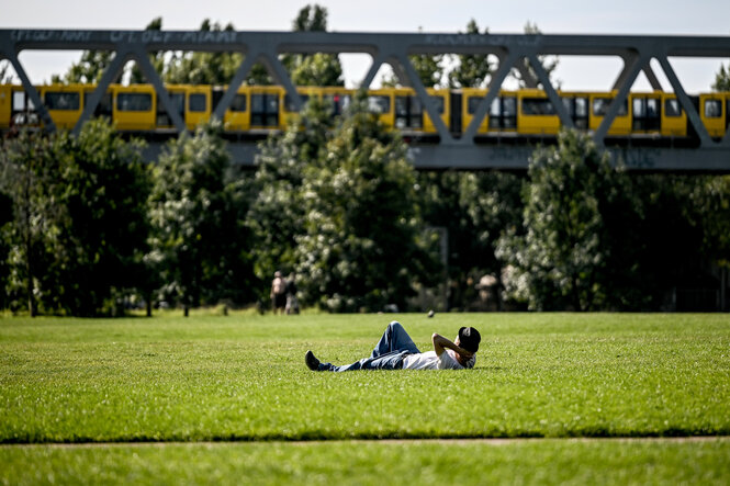Ein junger Mann liegt auf einer Wiese im Park am Gleisdreieck.