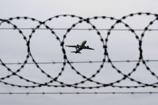 Ein Flugzeug startet - fotografiert durch Stacheldraht am Flughafenzaun.