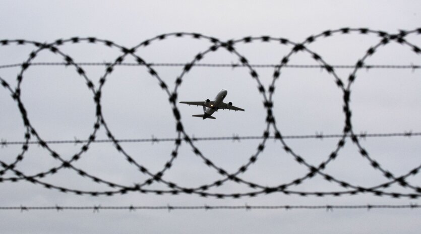 Stacheldraht vor Flugzeug im Himmel