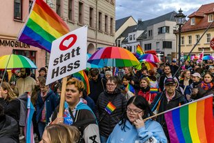 Menschen demonstrieren mit Regenschirmen und Fahnen in Regenbogenfarben