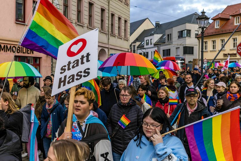 Menschen demonstrieren mit Regenschirmen und Fahnen in Regenbogenfarben