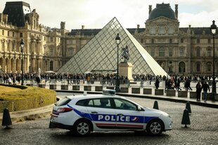 Ein Polizeiauto parkt im Hof des Louvre, während Besucher vor der Glaspyramide in einer Schlange stehen