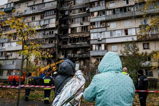 Menschen stehen vor den zerstörten Wohnungen eines Hauses