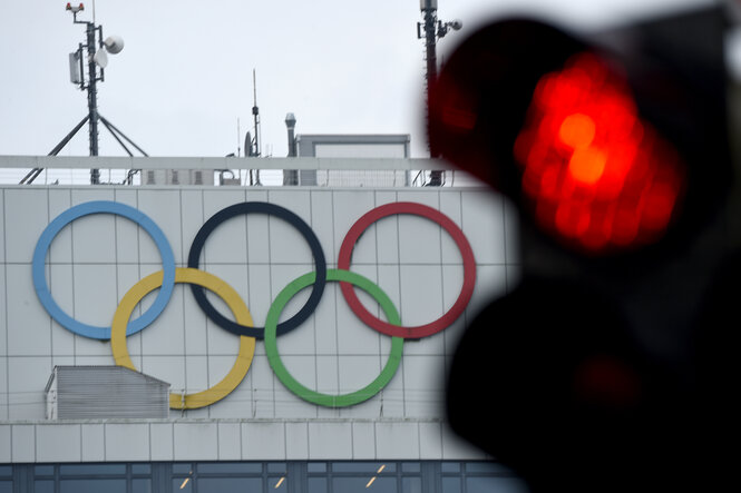 eine Rote Ampel vor einem Hochhaus, an dessen Fassade die olymischen Ringe hängen
