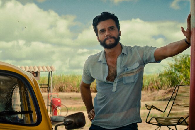 Ein Mann stützt sich an einer Säule ab, hinter ihm ist ein Feld zu sehen