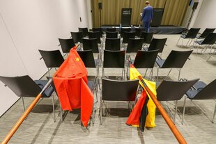 Eine chinesische (l) und eine deutsche Nationalflagge liegen über Stühlen in einem Raum, der für Pressekonferenzen gedacht scheint