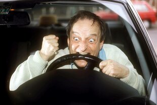 Fluchender Autofahrer beißt wütend ins Lenkrad