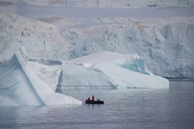 Das Bild zeigt zwei Personen auf einem Boot zwischen Eisbergen.