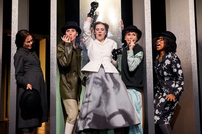 Frauen mit Hüten vor einer gitterartigen Kulisse