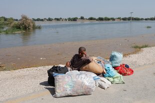 Ein Junge sitzt mit seinen Habseligkeiten an den Ufern eines Flusses, der Hochwasser führt