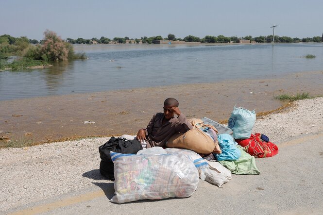 Ein Junge sitzt mit seinen Habseligkeiten an den Ufern eines Flusses, der Hochwasser führt