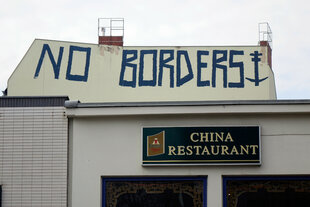 Das Bild zeig ein chinesisches Restaurant von Außen. Über dem Restaurant steht mittels eines Graffiti "NO BORDERS"auf einer Hochhauswand geschrieben.