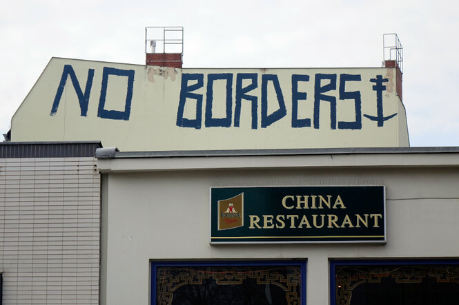 Das Bild zeig ein chinesisches Restaurant von Außen. Über dem Restaurant steht mittels eines Graffiti "NO BORDERS"auf einer Hochhauswand geschrieben.
