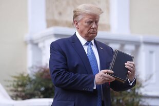Trump hält eine Bibel in den Händen und schaut sie skeptisch an