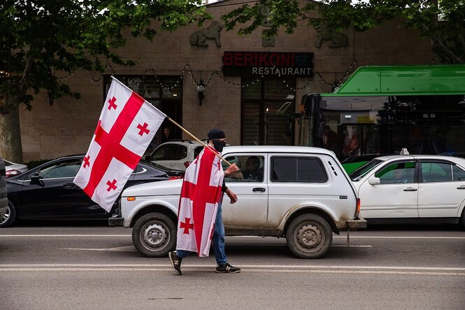 Ein Mann mit zwei Landesfahnen von georgien läuft über eine stark befahrene Straße